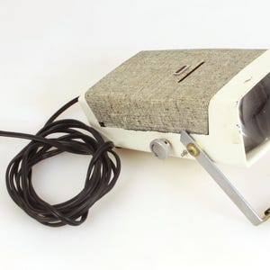 Puede incluir: Foco vintage con cuerpo color crema, parte superior gris texturizada y lente transparente. Tiene un soporte de metal plateado y un cable de alimentación negro. El foco presenta una perilla y una ranura en la parte superior.