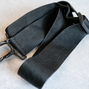 Puede incluir: Correa de hombro ajustable negra con cierres metálicos. La correa está hecha de material de nylon tejido.