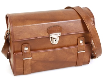 May include: A brown leather camera bag with a metal clasp and a shoulder strap.