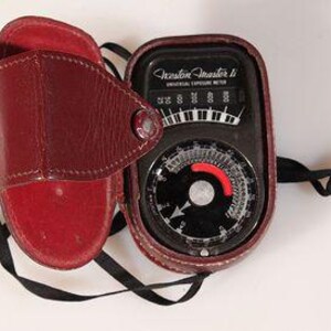 May include: A vintage Weston Master II Universal Exposure Meter with a leather case. The meter has a black face with white markings and a red indicator needle. The case is a deep red color and has a strap.