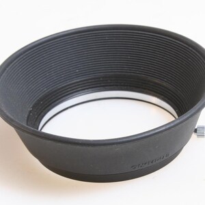 May include: A black rubber lens hood with a white inner ring and a silver screw on the side. The lens hood is designed to prevent glare and unwanted light from entering the lens.