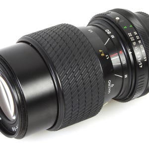 Puede incluir: Un objetivo Tokina 80-200 mm f/4,5-5,6 negro con ajuste macro. El objetivo tiene una empuñadura de goma negra y un anillo plateado con marcas para la apertura y la distancia focal.