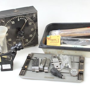 May include: A collection of vintage tools and equipment, including a black timer with a large dial, a funnel, and a black and silver device. Also included are a tray of tools, a container with tools, and a small yellow box.