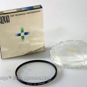 May include: A Hoya camera filter set, comprising a filter, a clear plastic case, and the original box. The box is beige with the Hoya logo and the text "FOR TECHNICAL PHOTOGRAPHY". The filter has a black rim and clear glass.