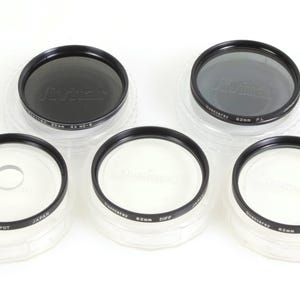 Könnte beinhalten: Fünf 62 mm Objektivfilter in durchsichtigen Plastikboxen. Die Filter sind mit "Hoya", "62 mm PL", "62 mm C.E", "62 mm DIFF" und "62 mm SPOT" beschriftet.