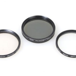 May include: Three black camera lens filters, each with a different function. The filters are 52mm in diameter. The first filter is a polarising filter, the second is a skylight filter, and the third is a diffuser filter.