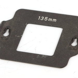 May include: A black metal frame with a rectangular opening labeled "135mm". The frame has two small hooks on each side.