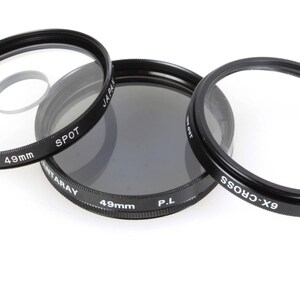 May include: Three black camera lens filters, each with a 49mm diameter. The filters are labeled "Spot", "P.L." and "GX-Cross".