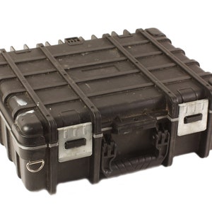 Puede incluir: Una maleta de transporte rígida negra con un cierre plateado y un asa. La maleta tiene una superficie texturizada y está hecha de plástico duradero.