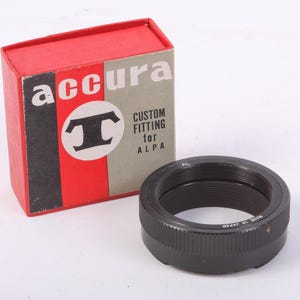 May include: A black Accura custom fitting for ALPA camera lens adapter with a red and gray box. The box has the Accura logo and text. The adapter is made in Japan.