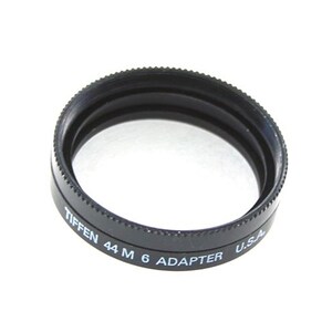 May include: A black Tiffen 44 M 6 Adapter filter ring for camera lenses. The ring is made of plastic and has a black finish. It is labelled "Tiffen 44 M 6 Adapter U.S.A."