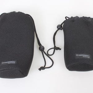 Puede incluir: Dos bolsas negras de malla con cordón. Las bolsas tienen forma cilíndrica y están hechas de un material de malla transpirable. Cada bolsa tiene un cierre de cordón con una cuenta negra y una pequeña etiqueta con texto. Las bolsas están diseñadas para guardar objetos pequeños.