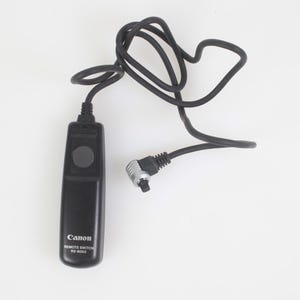 May include: Black Canon Remote Switch RS-80N3 with a coiled black cable and a silver-toned connector. The remote has a large, round button and the Canon logo. Ideal for photographers needing remote camera control.