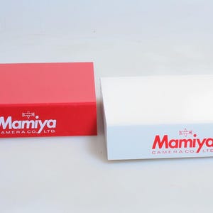 May include: Two rectangular boxes, one red and one white, with the Mamiya Camera Co. LTD logo printed on the front.