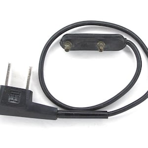 May include: A black electrical cord with a two-prong plug and a two-pin connector. The cord is looped, and the plug has two metal prongs. The connector has two metal pins.