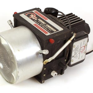 Może przedstawiać: Czarny i srebrny kondensator zmienny z napisem "Variable Condenser" i "Sylvania" na górze. Kondensator ma srebrny element cylindryczny i czarny prostokątny korpus z czerwonymi akcentami. Z boku wystaje przewód zasilający.