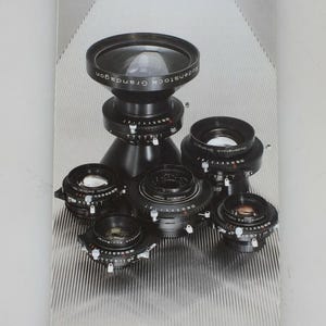 May include: A vertical brochure titled Camera lenses with the brand name Rodenstock at the bottom. The cover features a collection of five black Rodenstock camera lenses arranged in a cluster, showcasing their metallic barrels and glass elements.