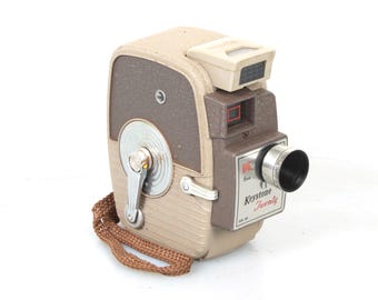 May include: A vintage Keystone Twenty 8mm film camera with a brown and beige body, a silver winding knob, and a black lens. The camera has a strap and the text "Keystone Twenty" is printed on the side.