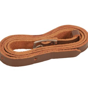 May include: A brown leather camera strap with a silver buckle. The strap is coiled and ready to be attached to a camera.