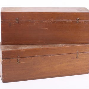 May include: Two wooden storage boxes stacked on top of each other. The boxes are rectangular with hinged lids and metal clasps. The wood has a warm brown tone with visible grain and some wear.
