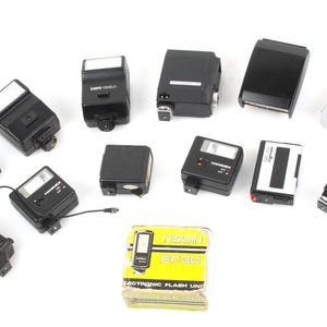 May include: A collection of vintage black flash units for cameras, including a Nissin EF30 electronic flash unit in its original box.