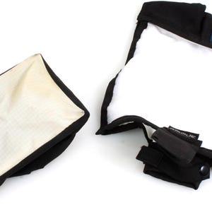 May include: Two softboxes for photography. One is closed, rectangular, with a white interior and black trim. The other is open, square, with a white interior and black trim. Both have black straps and fasteners.