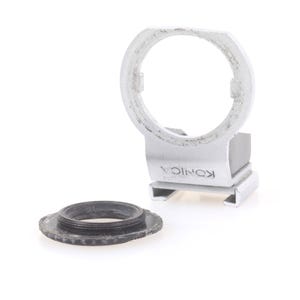 May include: A silver Konica camera lens adapter with a circular opening and a separate black lens ring. The adapter has the Konica brand name printed on it. The items are on a white background.