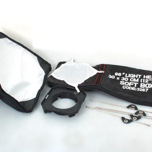 Könnte beinhalten: Ein schwarzer Softbox-Lichtkopf mit einem weißen Diffusor und einer schwarzen Tragetasche. Die Softbox ist 30 cm x 30 cm groß und hat den Code 3267.