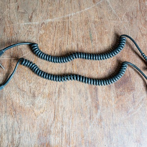 May include: Two black coiled cords with plugs on each end. One cord has a standard plug and the other has a smaller, round plug.