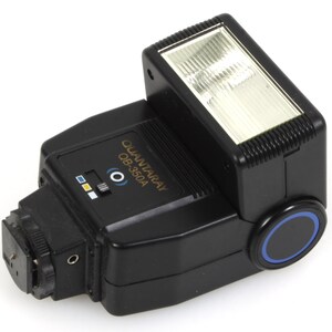 May include: A black Quantaray QB-350A camera flash unit. The flash has a rectangular head with a clear, textured front. The body features a control panel with various settings and a circular blue accent. The flash is designed to attach to a camera.