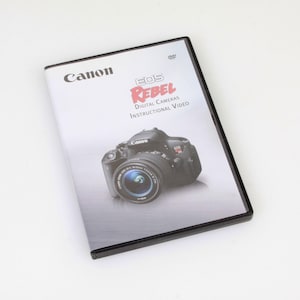 May include: A black Canon EOS Rebel digital camera instructional video DVD case. The case features a photo of a black Canon EOS Rebel camera with a silver lens.