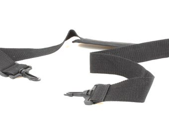 May include: Black nylon strap with two plastic clips. The strap is designed to be adjustable and features a padded section for comfort. The clips are designed to attach to a bag or other item.