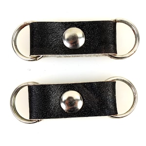以下が含まれることがあります： 銀色の金属製のリングと丸い銀色の金属製のスタッドが付いた黒い革のストラップ2本。ストラップはサスペンダーまたはガーターとして使用するために設計されています。