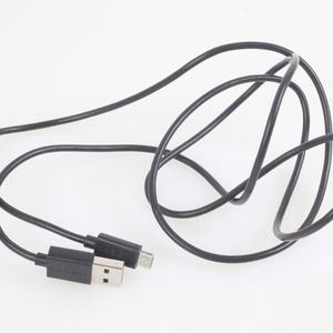 Op de afbeelding: Zwarte USB-oplaadkabel met een USB-A- en USB-C-connector. De kabel is opgerold en ligt op een witte ondergrond. De connectoren zijn zwart.