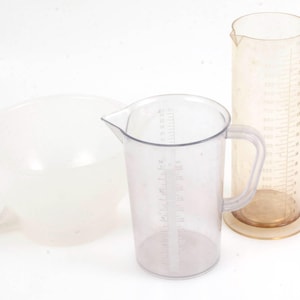 Könnte beinhalten: Drei transparente Messbecher aus Kunststoff. Der größte Becher ist ein Messzylinder mit Markierungen in Unzen. Der mittlere Becher ist ein Krug mit Henkel und Markierungen in Unzen. Der kleinste Becher ist eine Schüssel mit Henkel.