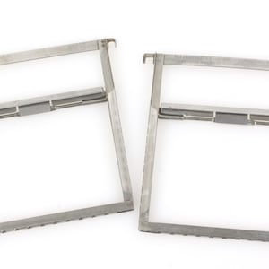 May include: Two silver metal frames with a rectangular shape and a small metal bar across the middle. The frames are made of thin metal and have a slightly textured surface.