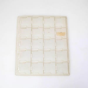 May include: A rectangular, off-white plastic storage tray featuring a grid of twenty individual square compartments arranged in four columns and five rows, designed for organising small items, with a small rectangular adhesive label on one slot.