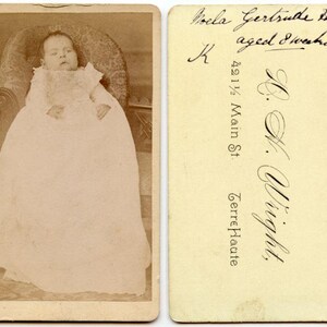 Op de afbeelding: Een sepia-kleurige vintage foto van een baby in een lange witte jurk zittend in een stoel met patroon. De achterkant bevat handgeschreven tekst: Nola Gertrude Hodges, aged 8 weeks, en de afdruk van de fotograaf: L. H. Wright, 421 1/2 Main St.