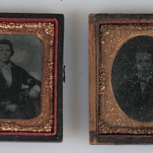 May include: Two antique daguerreotype portraits in rectangular cases. The left case features a rectangular gold-toned frame with a portrait of a person in a dark jacket. The right case has an oval gold-toned frame with a portrait of a person.