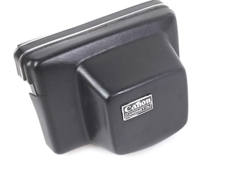 May include: Black camera case with the Canon and CANONET QL logo. The case is rectangular with rounded edges and a white trim. The case is made of a textured material and is designed to protect a camera.