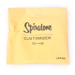 Puede incluir: Un sobre de papel amarillo claro con la palabra "Spiratone" en una fuente de estilo manuscrito. Debajo está la palabra "Customizer" y los números "58->49". La palabra "JAPAN" está impresa en la parte inferior.