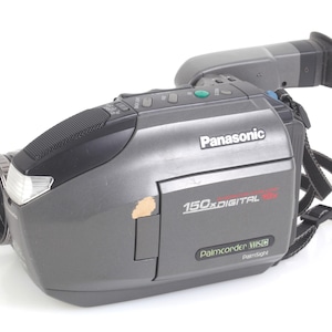 Könnte beinhalten: Grauer Panasonic Camcorder mit schwarzem Griff und Riemen. Auf dem Camcorder steht "150x DIGITAL" und "Palmcorder VHS". Der Camcorder hat ein schwarzes Objektiv und einen silbernen Blitz.