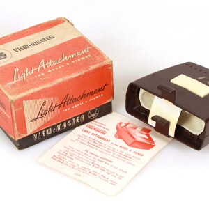 Könnte beinhalten: Vintage View-Master Lichtaufsatz für Modelle & Viewer. Die Box ist rot und beige mit schwarzem Text. Ein dunkelbrauner Viewer und ein Anleitungsblatt sind ebenfalls vorhanden. Ein Retro-Sammlerstück.