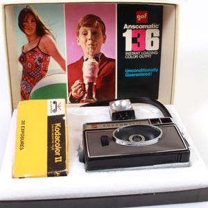 May include: A vintage Anscomatic 136 instant loading colour outfit camera with a black and silver body. The camera is in a box with a film cartridge labelled "Kodacolor II" and a picture of a woman in a swimsuit.