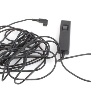 May include: Black camera remote control with a long, coiled cable. The remote has a rectangular body with a button and a connector at the end of the cable. The cable is approximately 91 cm long.