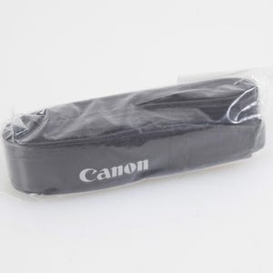 May include: A black camera neck strap featuring the white Canon logo printed on the fabric. The strap is folded and enclosed within a clear, thin plastic protective sleeve, maintaining its original shape and appearance for storage or transport.