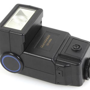 May include: A black Quantaray QB 6500A camera flash unit. The flash has a rectangular head with a clear, textured front. A circular blue and black accent is on the side. The flash is designed for use with cameras.