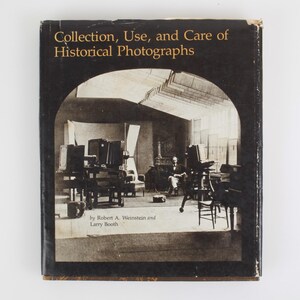 Puede incluir: Un libro de tapa dura titulado "Collection, Use, and Care of Historical Photographs" con una cubierta negra y letras doradas. La portada presenta una imagen en tonos sepia de un estudio fotográfico antiguo. Por Robert A. Weinstein y Larry Booth.