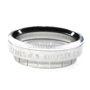 May include: A silver adapter ring with the text "SERIES # 5 ADAPTER RING" engraved on the side. The ring has a ridged edge and a black interior, set against a white background.
