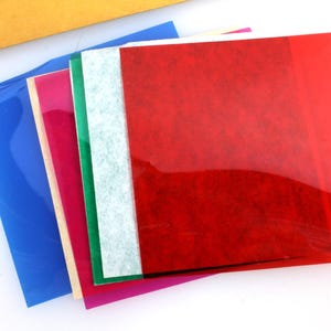 Puede incluir: Una pila de hojas de papel translúcidas de colores. La hoja superior es roja, la siguiente es verde, luego blanca, luego azul y la hoja inferior es rosa.